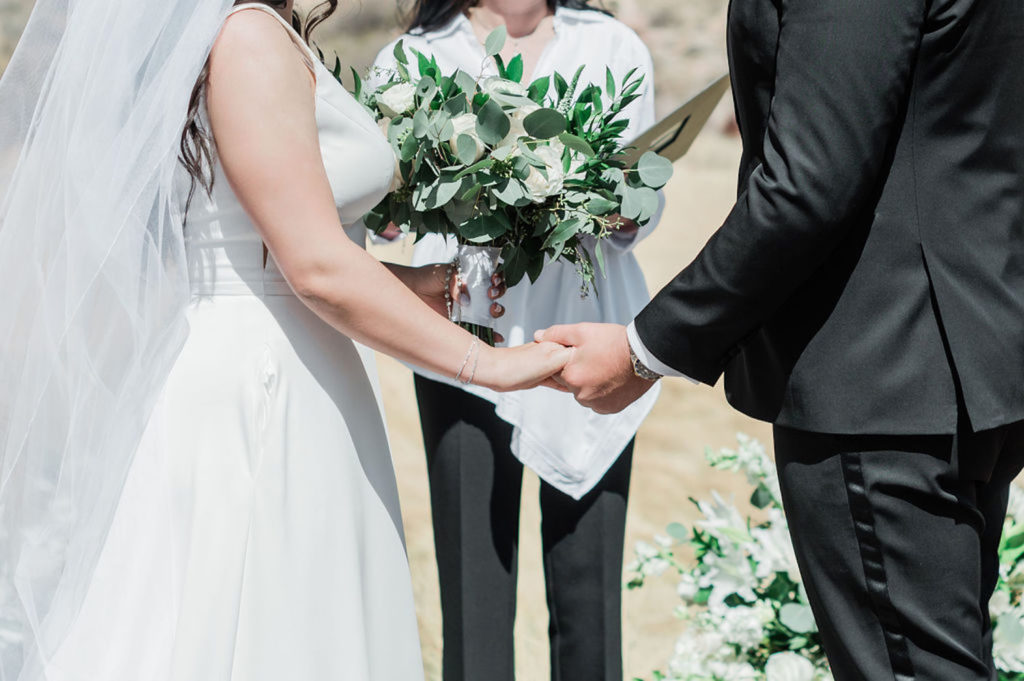 Close-up shot of bride and groom holding hands with the officiant in front of them during their elopement ceremony in Las Vegas