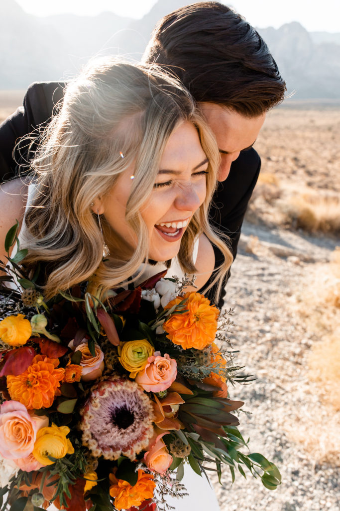 Groom hugging the bride from behind as they both share laughs during their Spring Mountain Ranch wedding shoot with Emily Reno