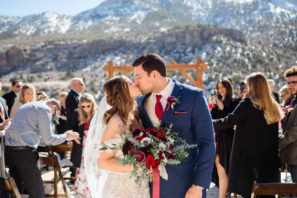 Newlywed couple sharing a kiss as they walk away from the aisle as their guests look on, captured by NV wedding photographer Emily Reno