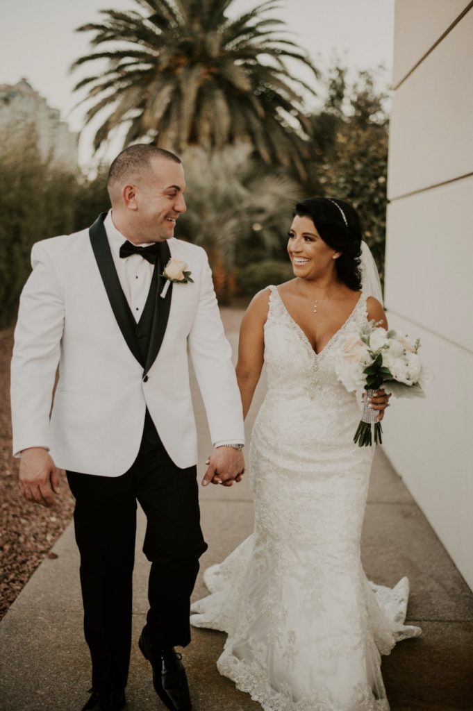 Bride and groom smiling at each other while holding hands and walking during their wedding shoot with Emily Reno