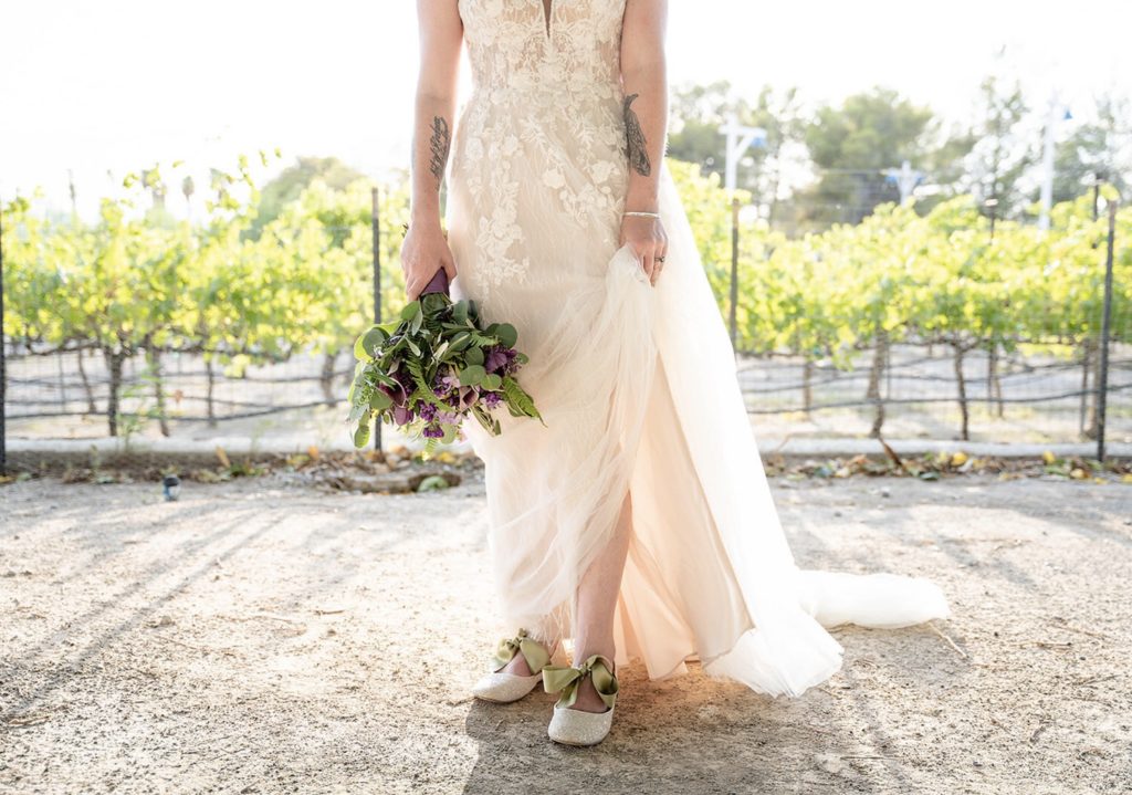 Close-up shot of the bride's lower half showing her stunning dress, vibrant purple and green bouquet and white shoes with green bows during their Las Vegas wedding shoot