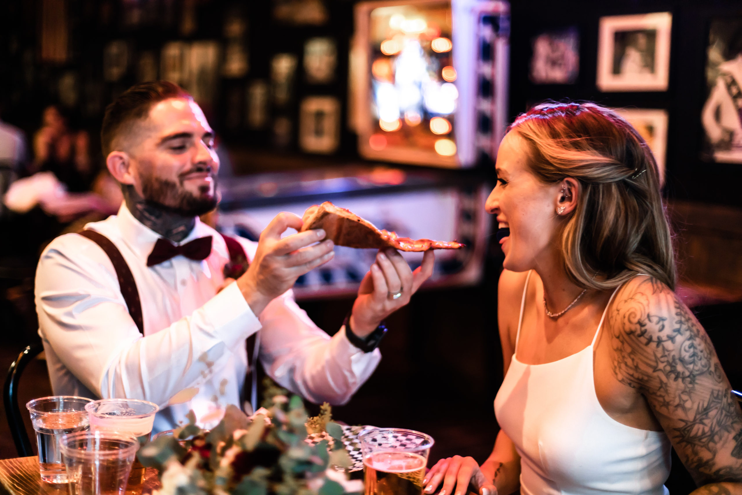 Groom smiles as he feeds a slice of pizza to his bride during their lavish dinner after their Las Vegas elopement