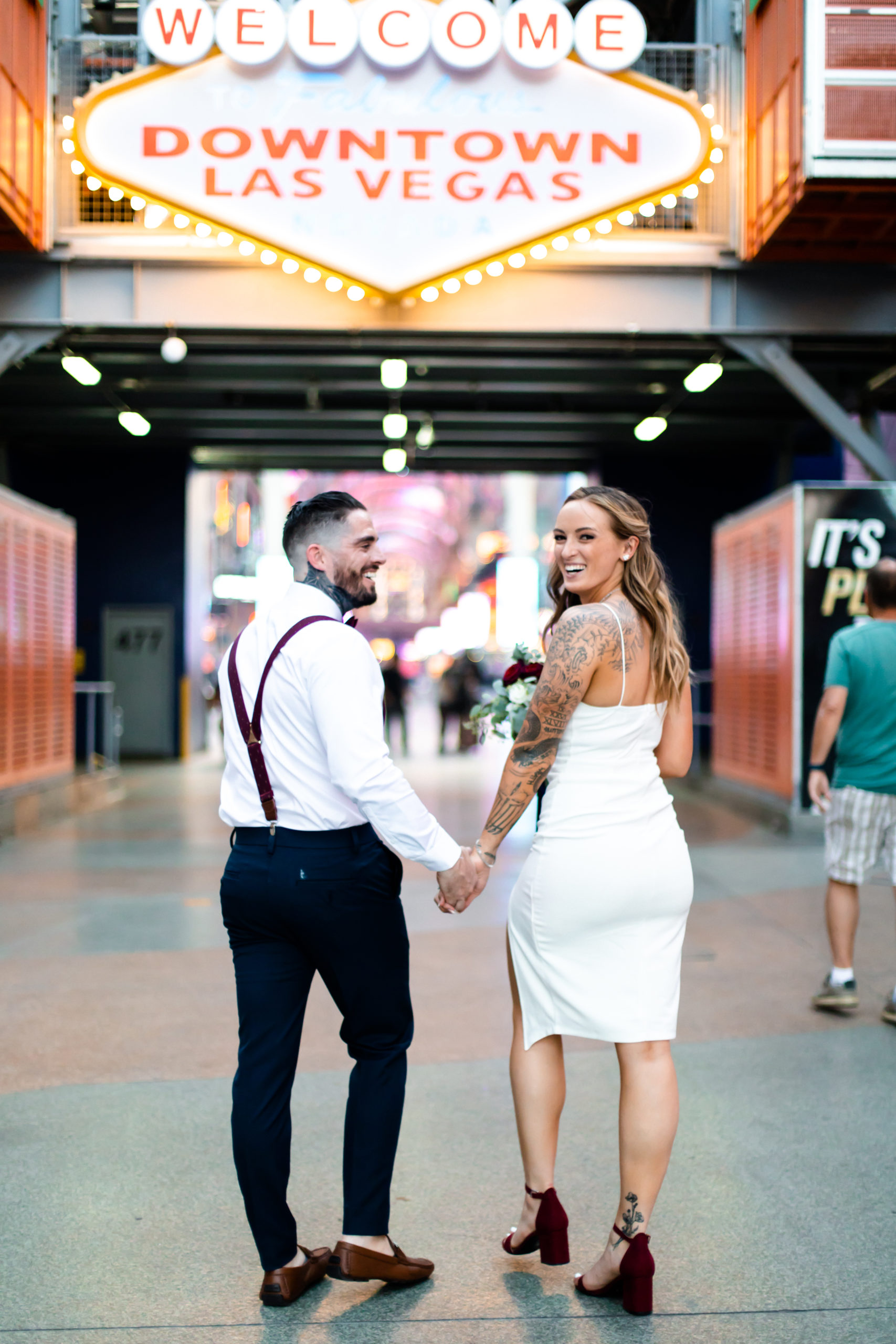 Bride and groom share a smile as they hold hands in front of the Welcome to Downtown Las Vegas sign during their elopement shoot