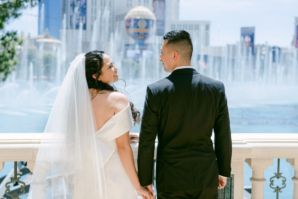 Bride and groom smiling as they hold hands in front of the fountain at The Bellagio in Las Vegas