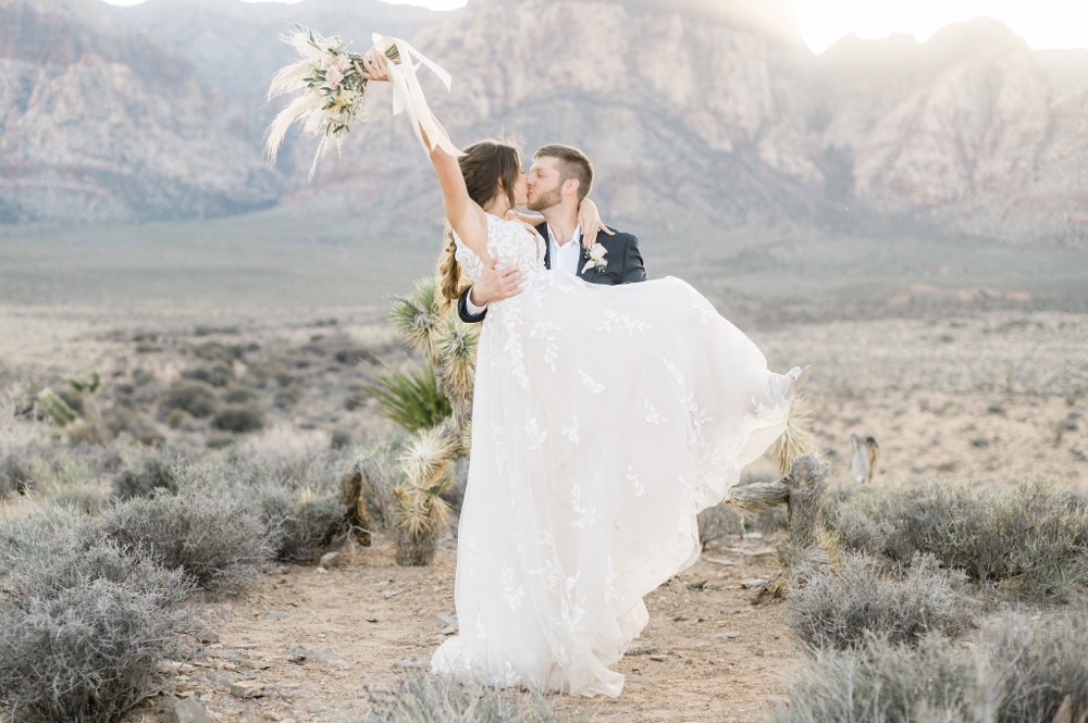 All Inclusive Elopement Packages:Groom lifts up bride as they share a kiss with bride raising her bouquet, captured by Elopement Las Vegas