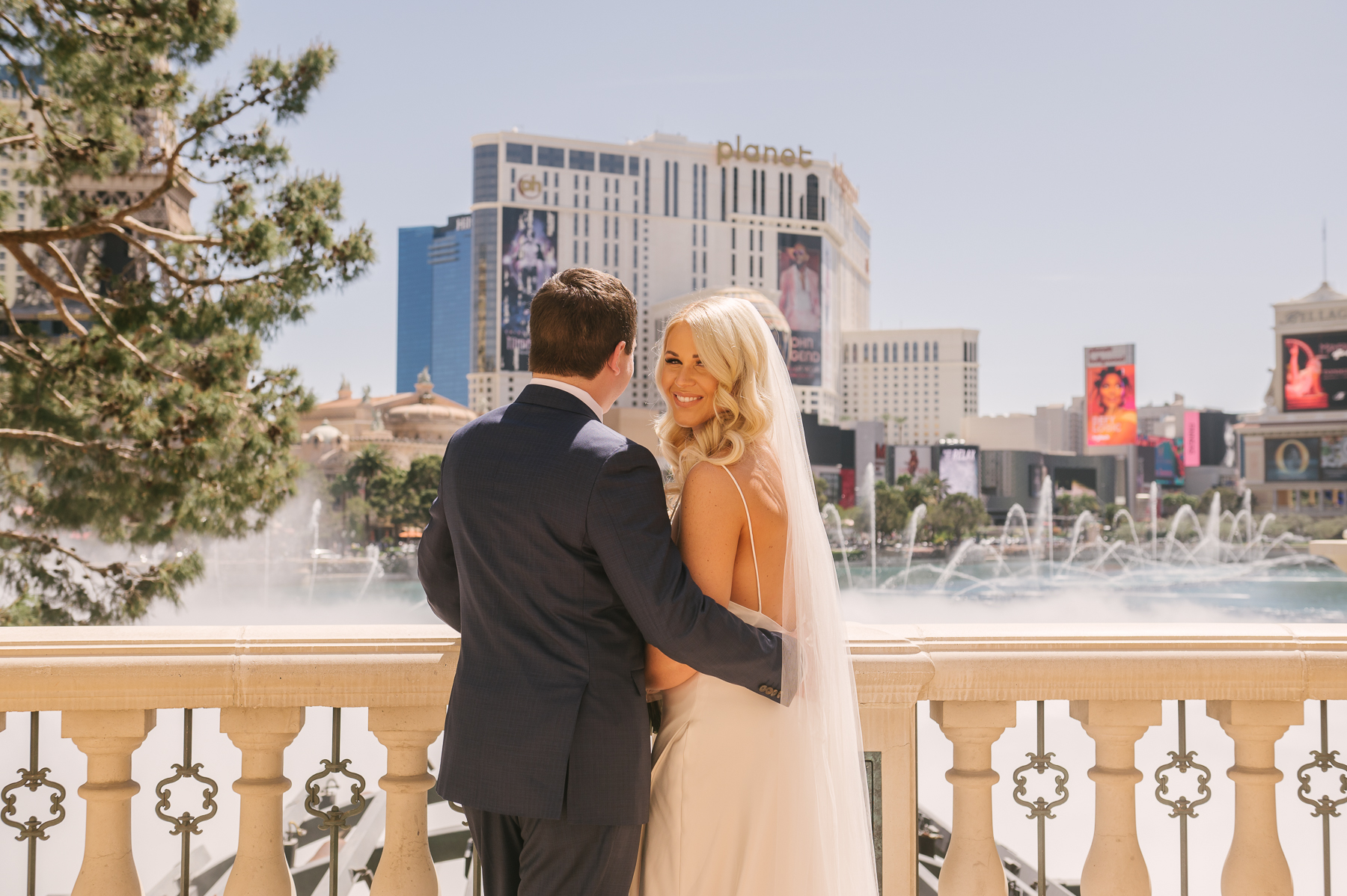 Bride smiling back at camera as groom wraps his arm around her at The Bellagio in Las Vegas