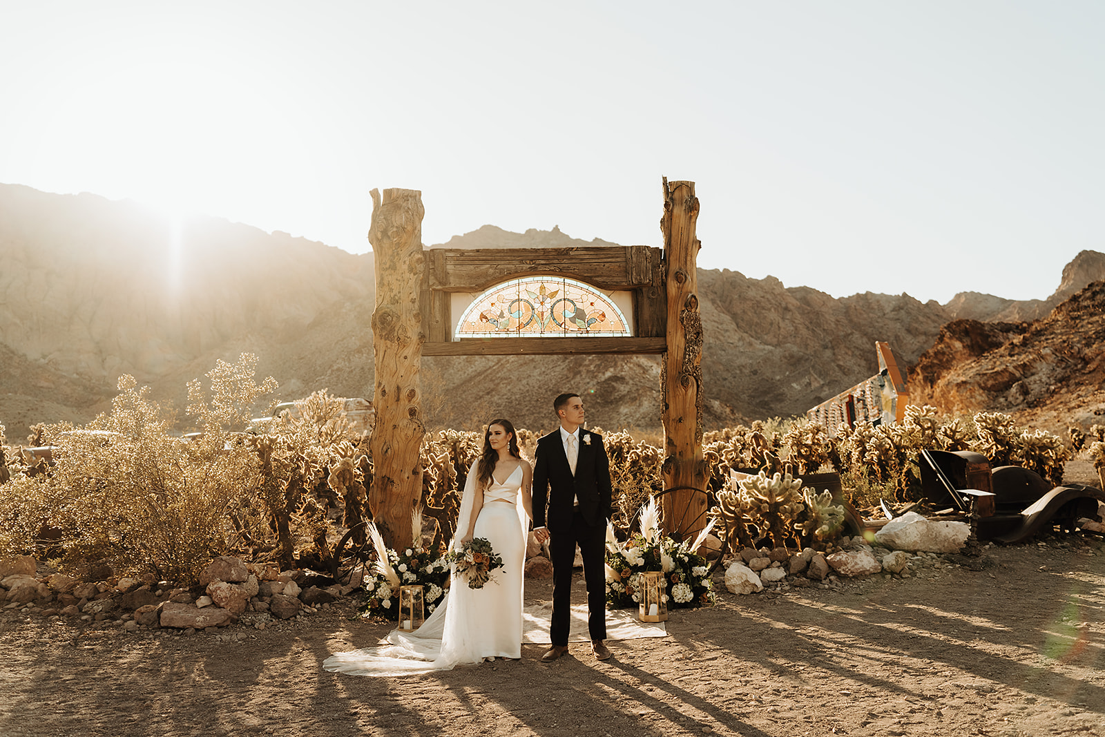 Bride and groom holding hands in front of arch at Nelson Ghost Town during their wedding shoot planned by Elopement Las Vegas