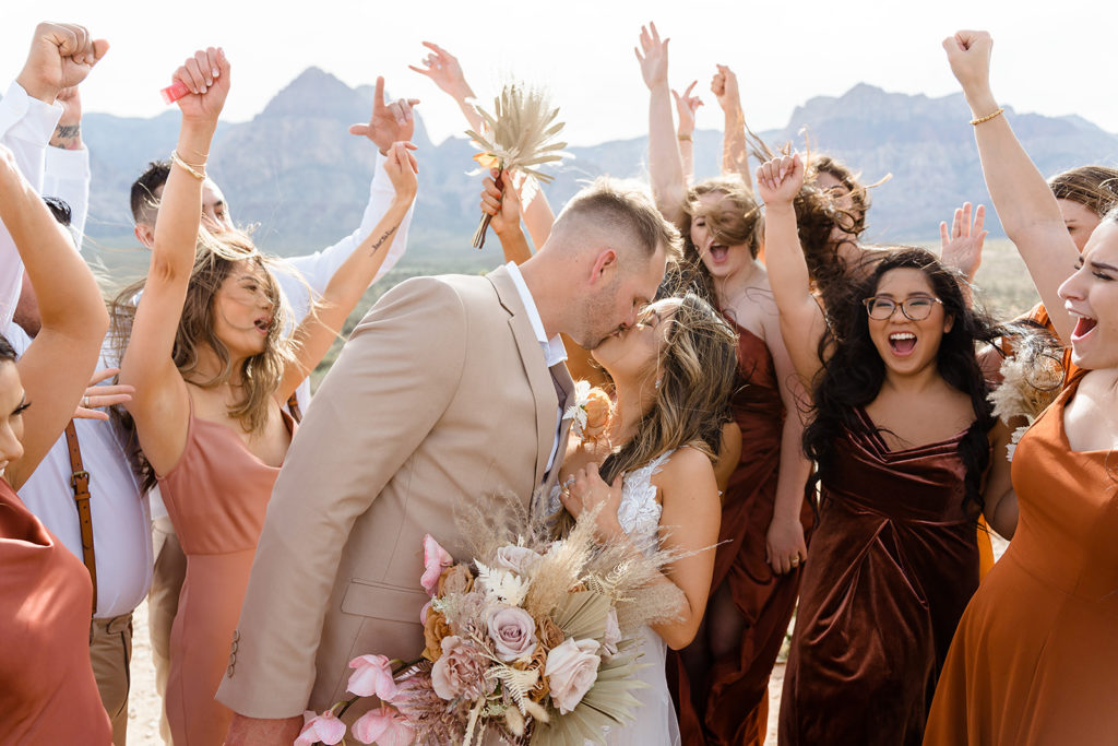 Bride and groom sharing a kiss as their entourage cheers during their Las Vegas elopement
