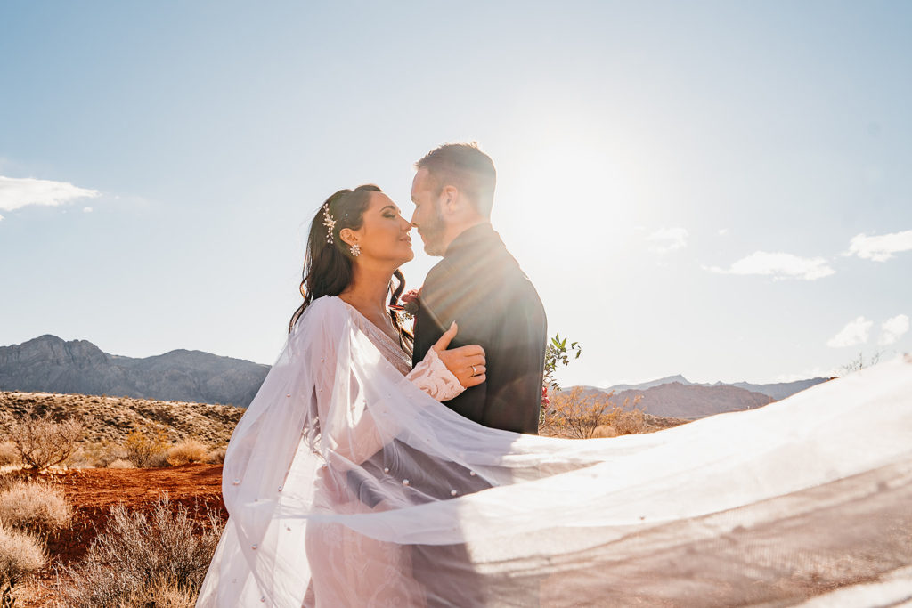 Valley of Fire Weddings - All-Inclusive Elopement Packages. Couple sharing an embrace with bride's veil swaying in the wind.