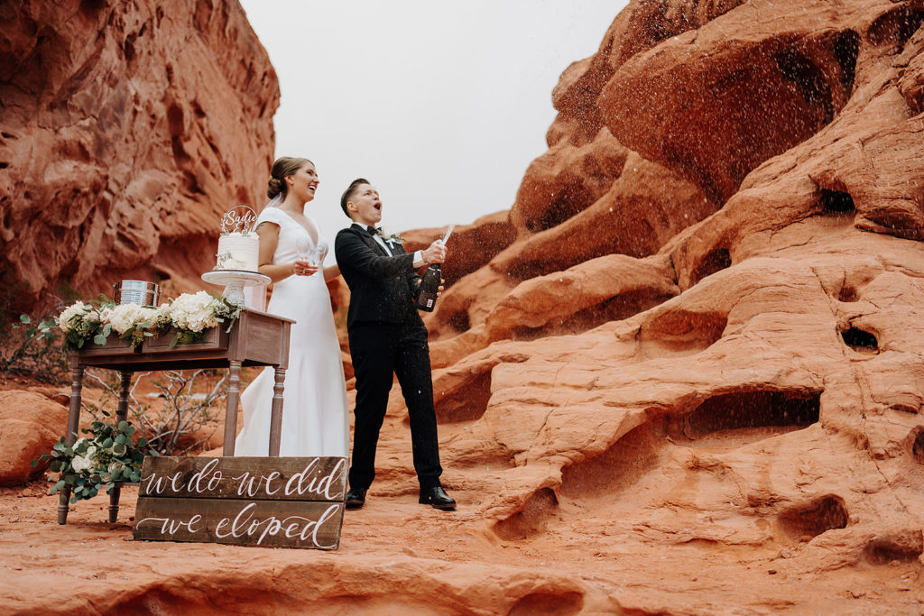 Couple smiling as they spray champagne next to their wedding cake at the Valley of Fire during their elopement planned by Elopement Las Vegas
