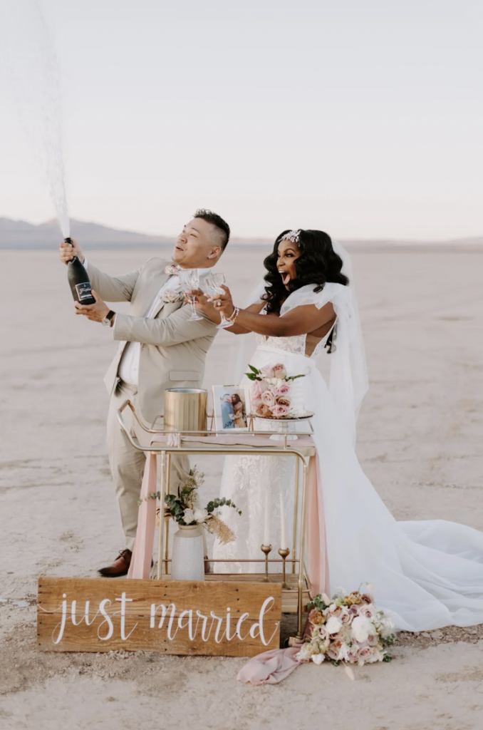 Bride and groom popping open a bottle of champagne at their wedding reception setup by Elopement Las Vegas