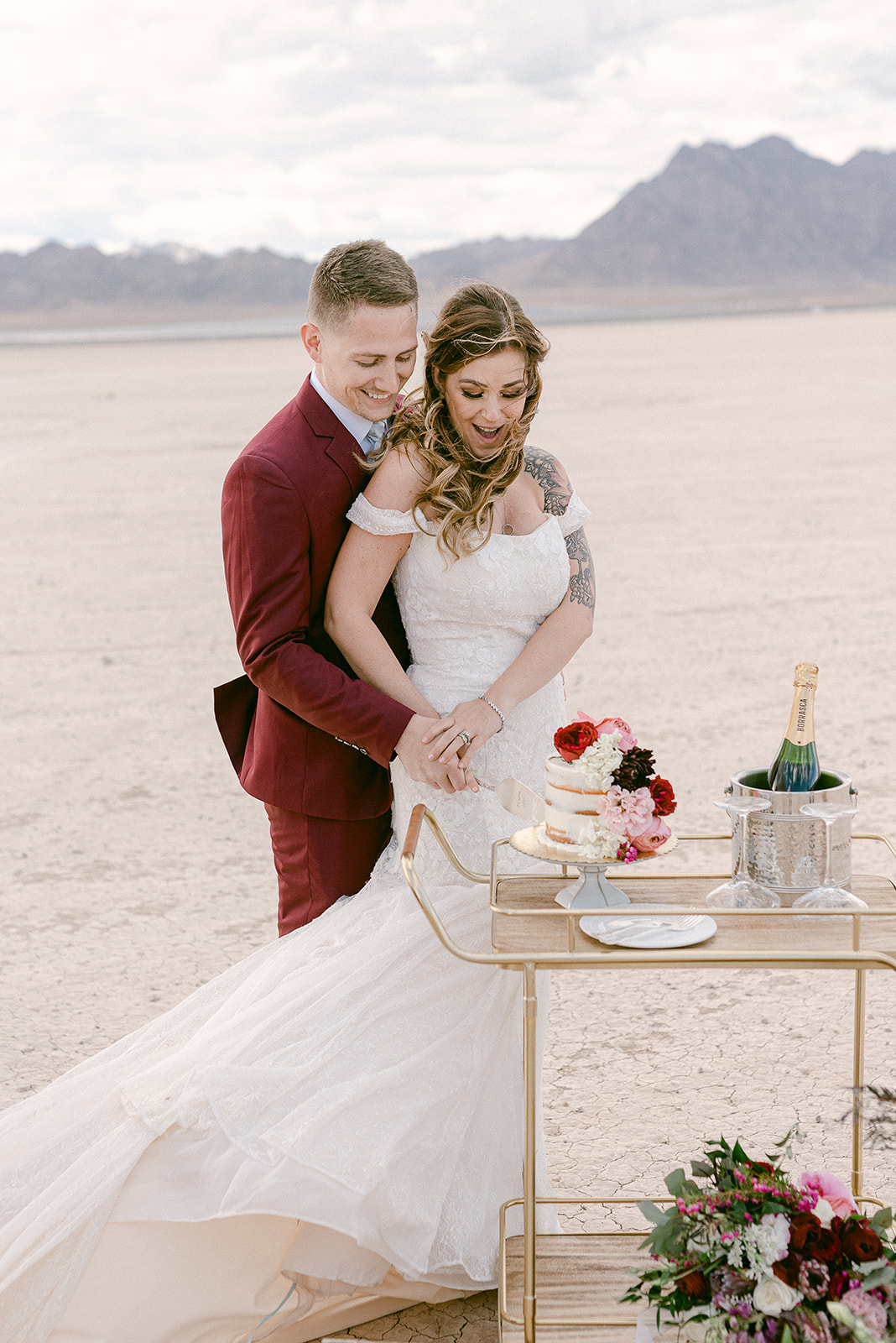 Bride and groom smiling as they cut a slice of their wedding cake during their Dry Lake Bed wedding reception