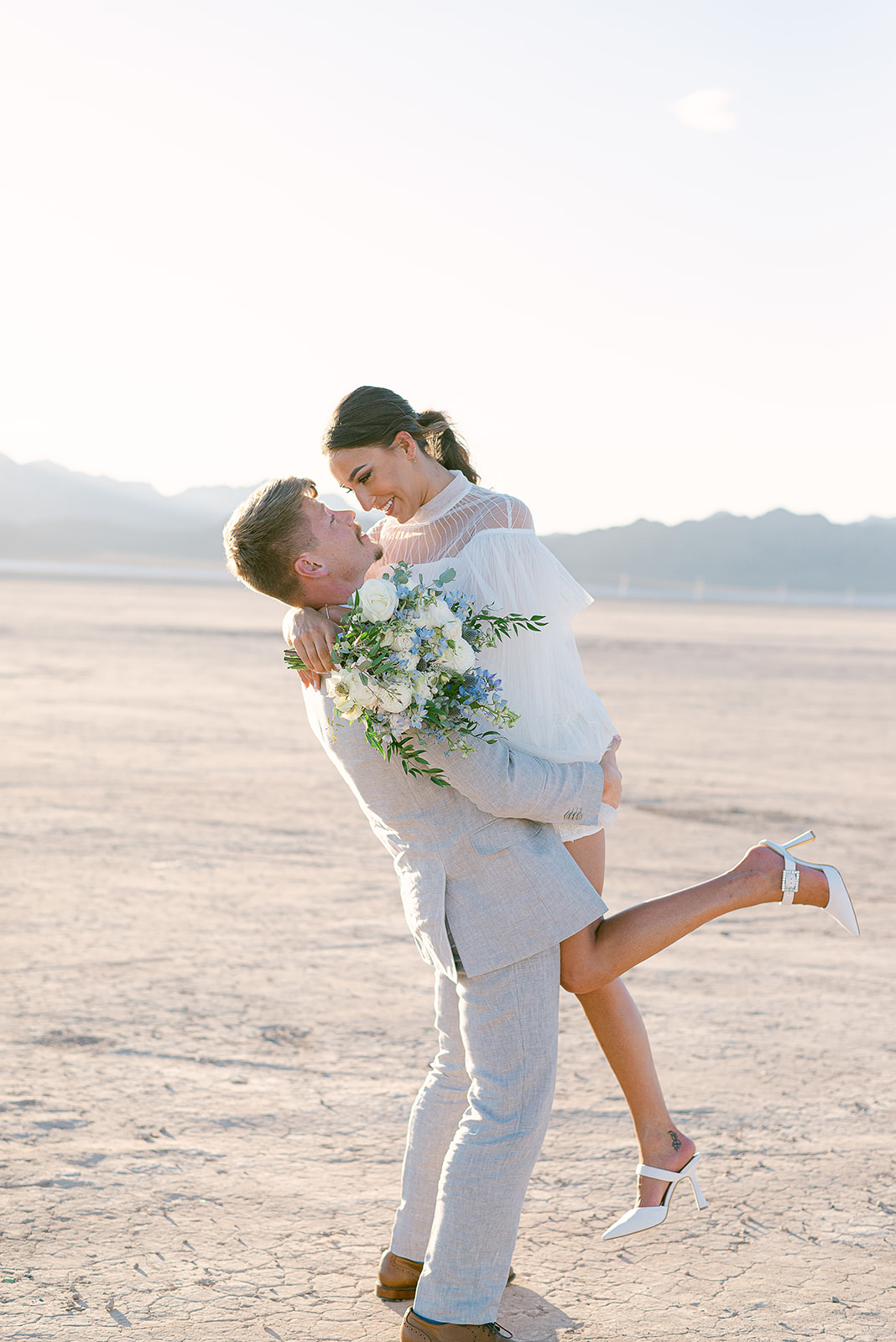 Groom lifts bride up as they smile at each other during their shoot organized by Elopement Las Vegas