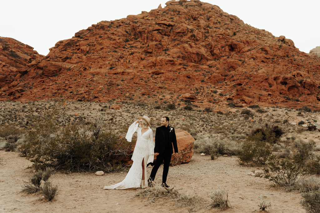 How To Plan The Perfect Red Rock Canyon Elopement (Las Vegas). Bride and groom holding hands with view of canyon behind them.