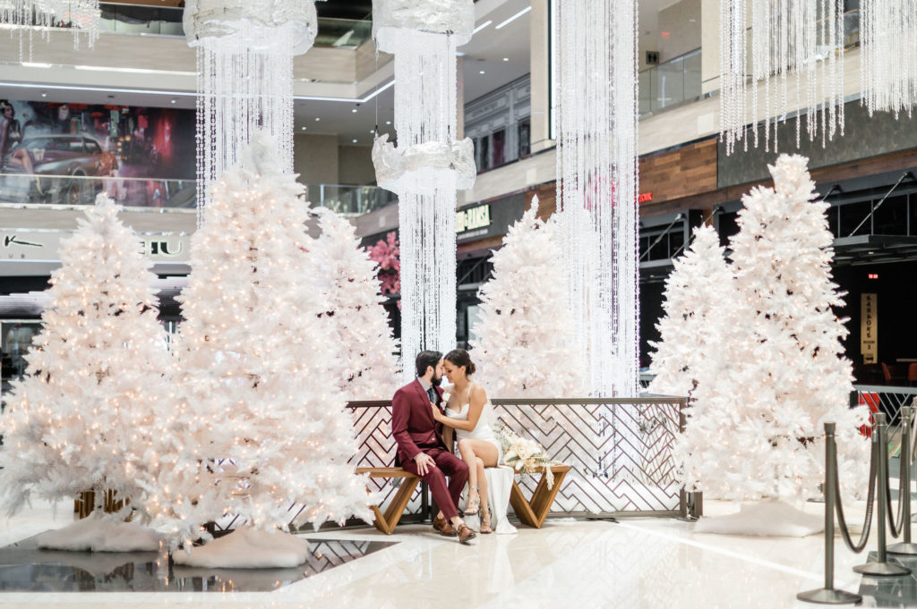 All Inclusive Resorts World Wedding Package (Las Vegas). Couple sitting on bench inside venue with Christmas trees.