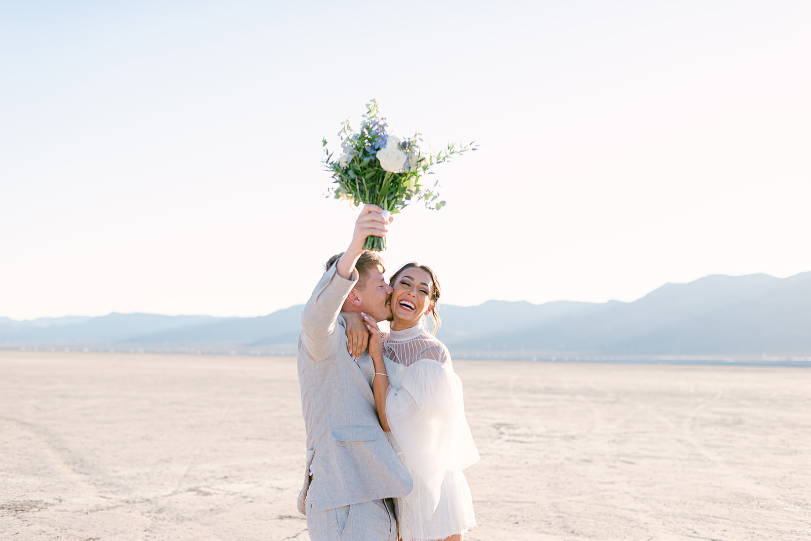 Groom holding up bride's bouquet as she wraps her arms around him during elopement shoot in Las Vegas