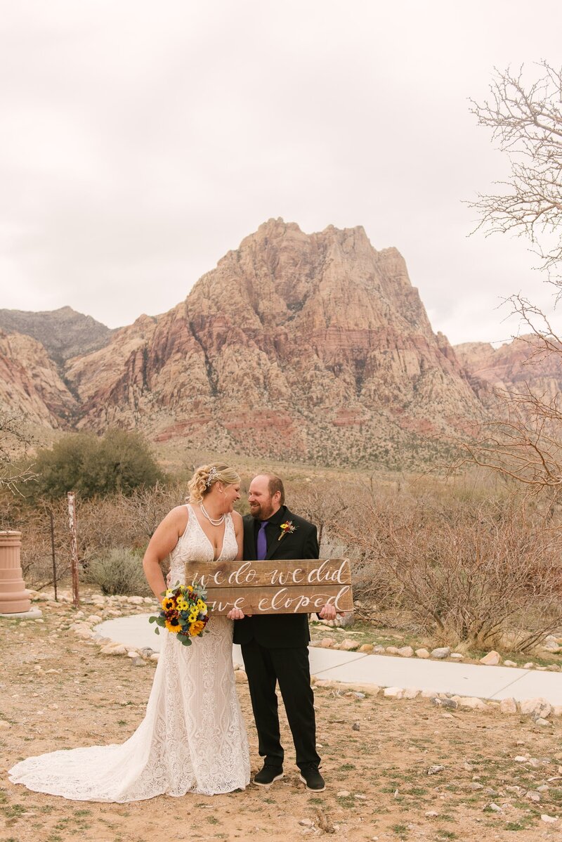 Couple smiling at each other as they hold up just eloped sign at Spring Mountain Ranch