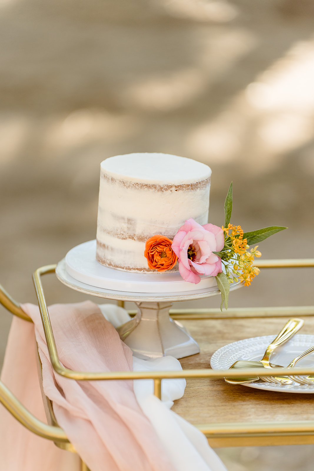 Wedding cake with vanilla frosting and flowers on tray next to gold utensils