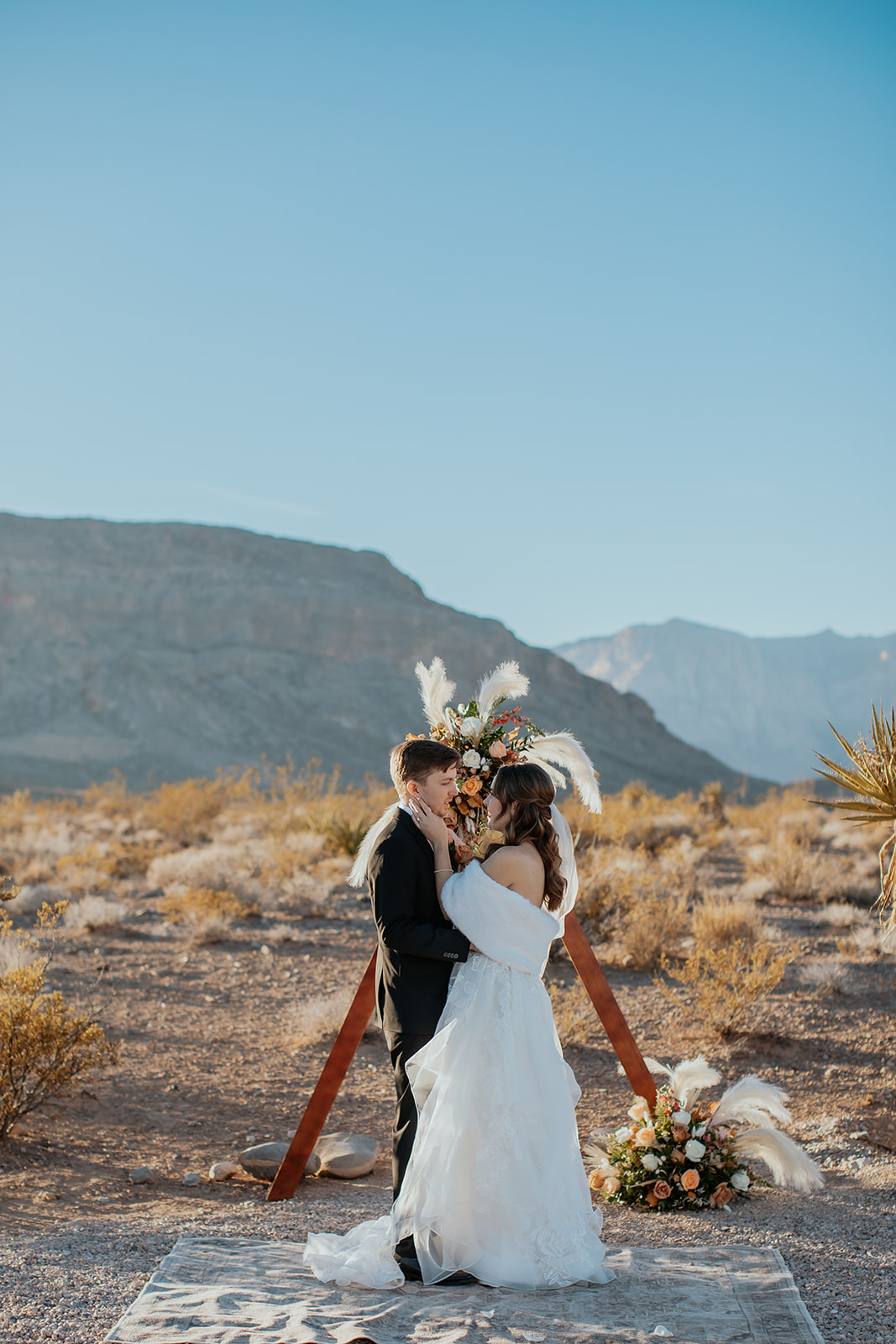 Bride and groom sharing an embrace in front of their wedding arch in the desert in Las Vegas