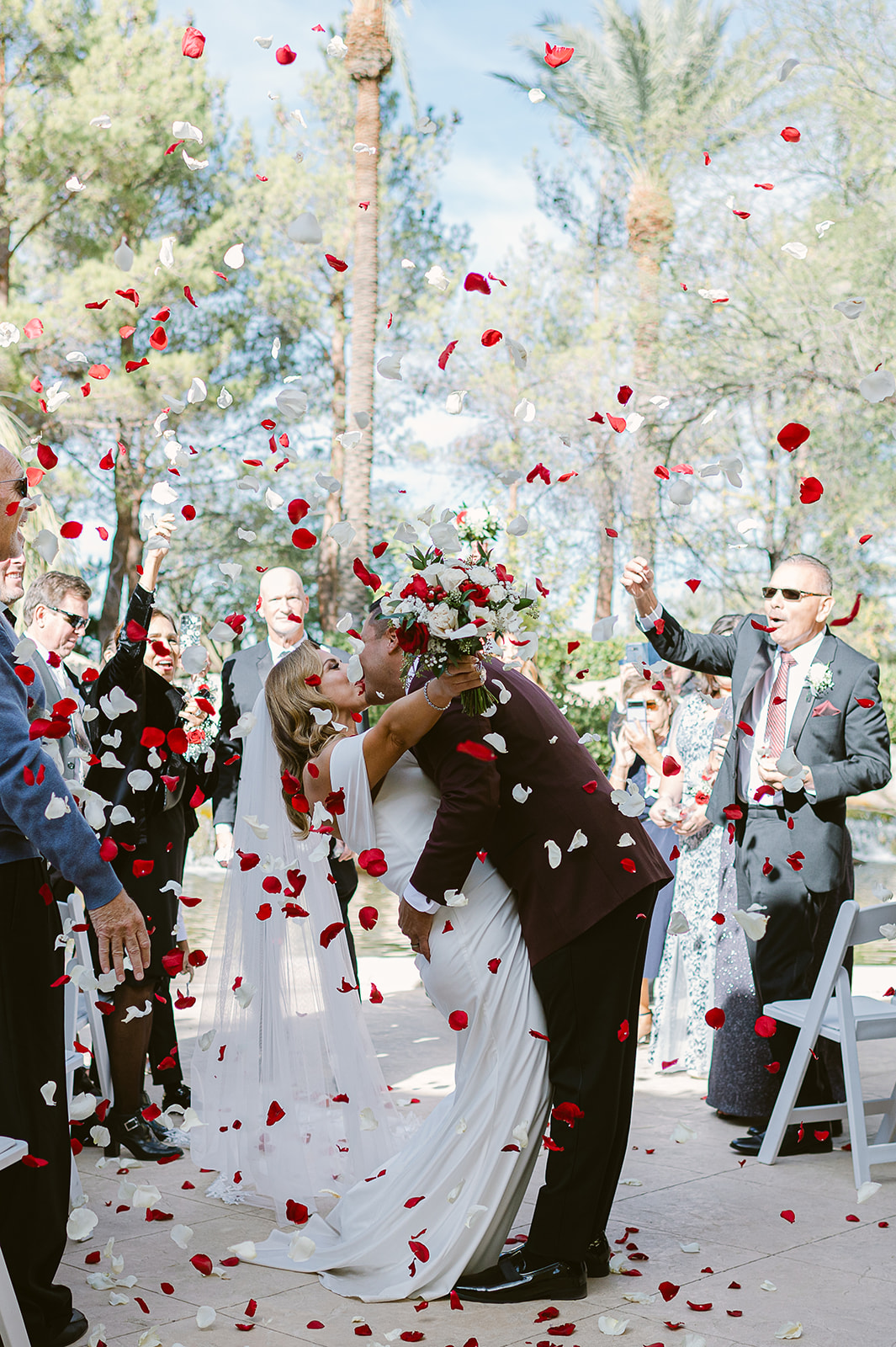 Newlywed couple sharing a kiss as their guests shower them with rose confetti in Las Vegas