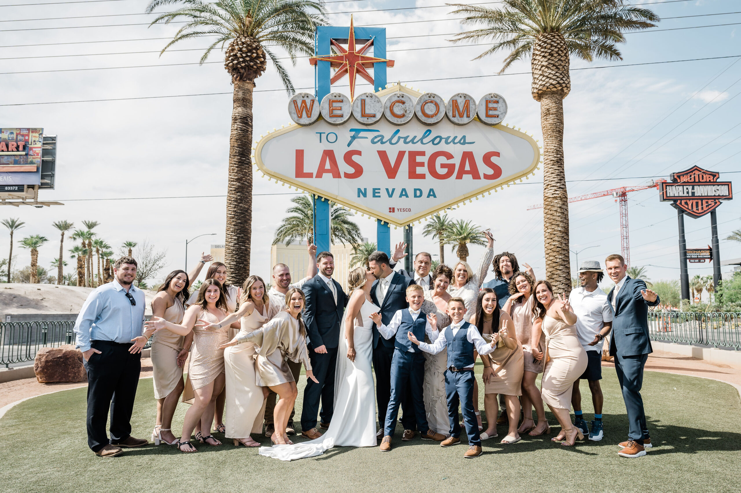 Bride and groom sharing a kiss during their wedding shoot with their family at the Las Vegas welcome sign