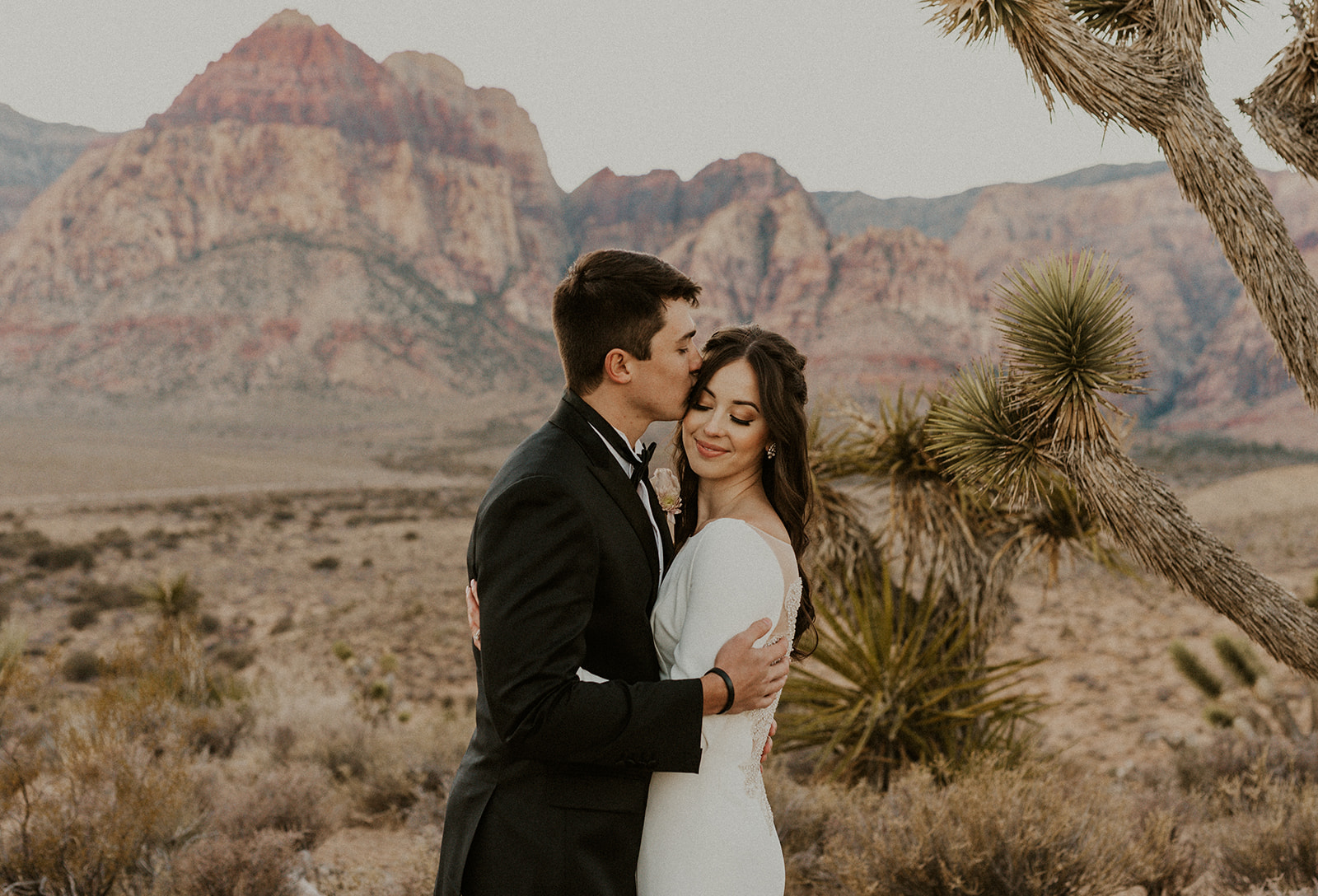 Groom planting a kiss on bride's temple as she smiles during their Las Vegas elopement shoot